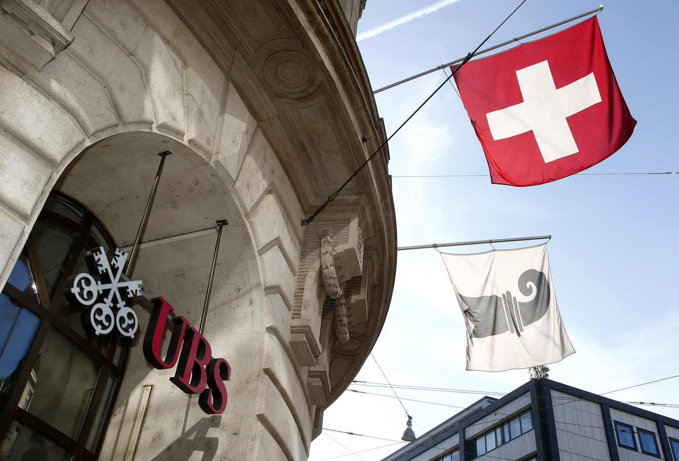 A Swiss national flag and a flag of the city of Basel fly over the entrance of a branch office of Swiss bank UBS in Basel